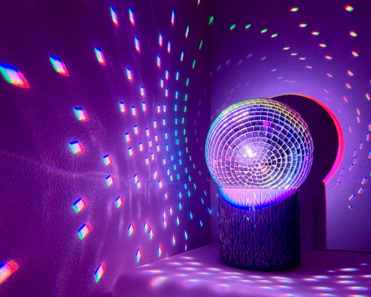 A small disco ball glowing on its stand, scattering rainbow-colored light across a purple-lit room.